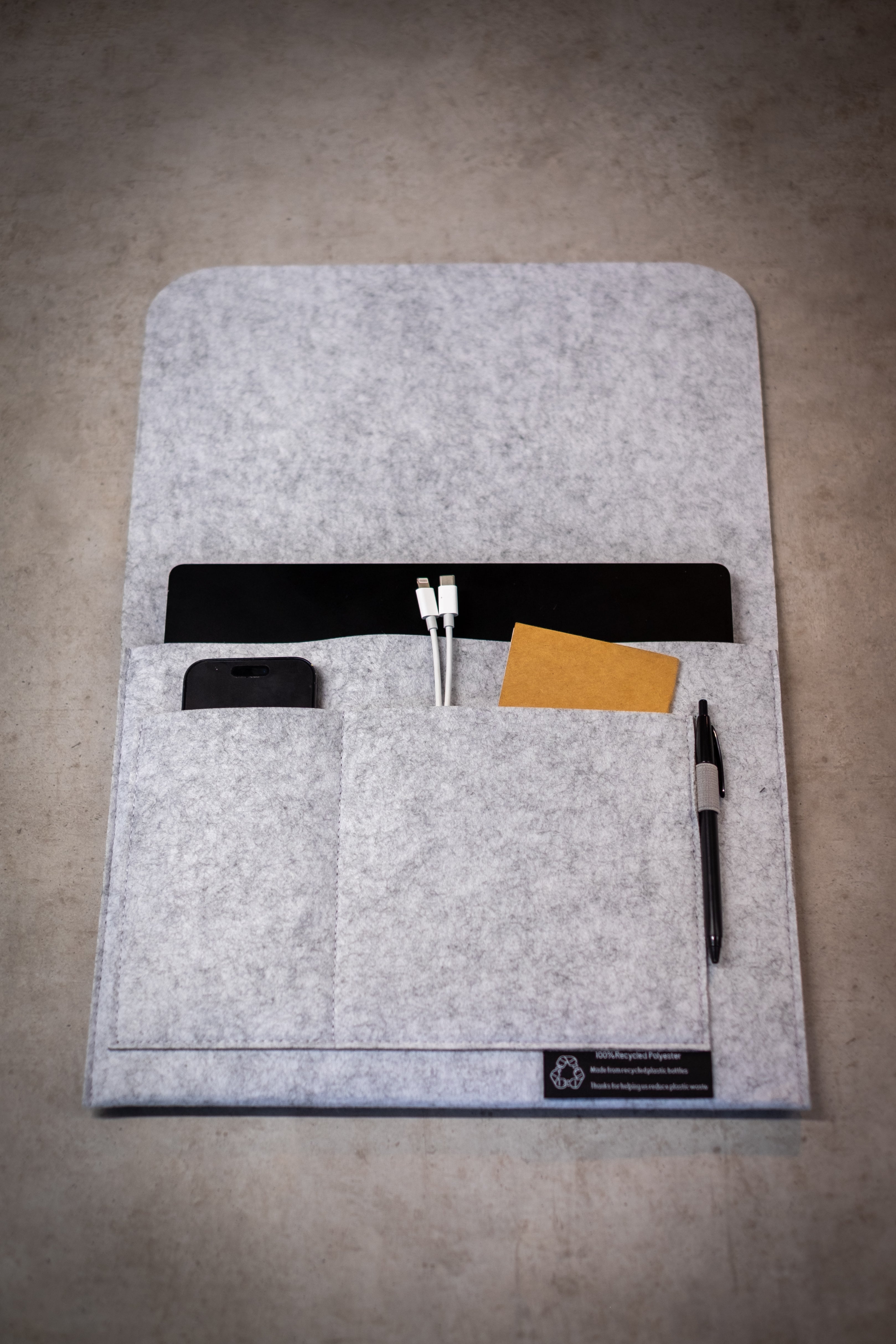 RMIT Store rPET Utility Laptop Sleeve in grey felt, made from 100% recycled polyester, featuring multiple organiser pockets for a laptop, phone, cables, stationery, and cards, with a stitched sustainability label on the front.